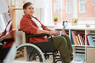 woman in wheelchair using a laptop in front of a bookshelf