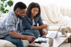 smiling black couple checking financial bills with a calculator and a laptop