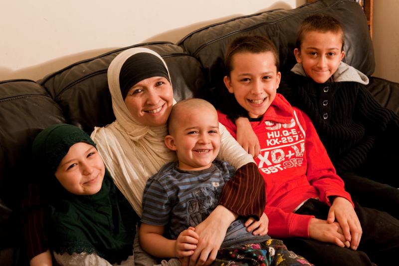 Woman smiling, wearing head covering and sitting with her four children